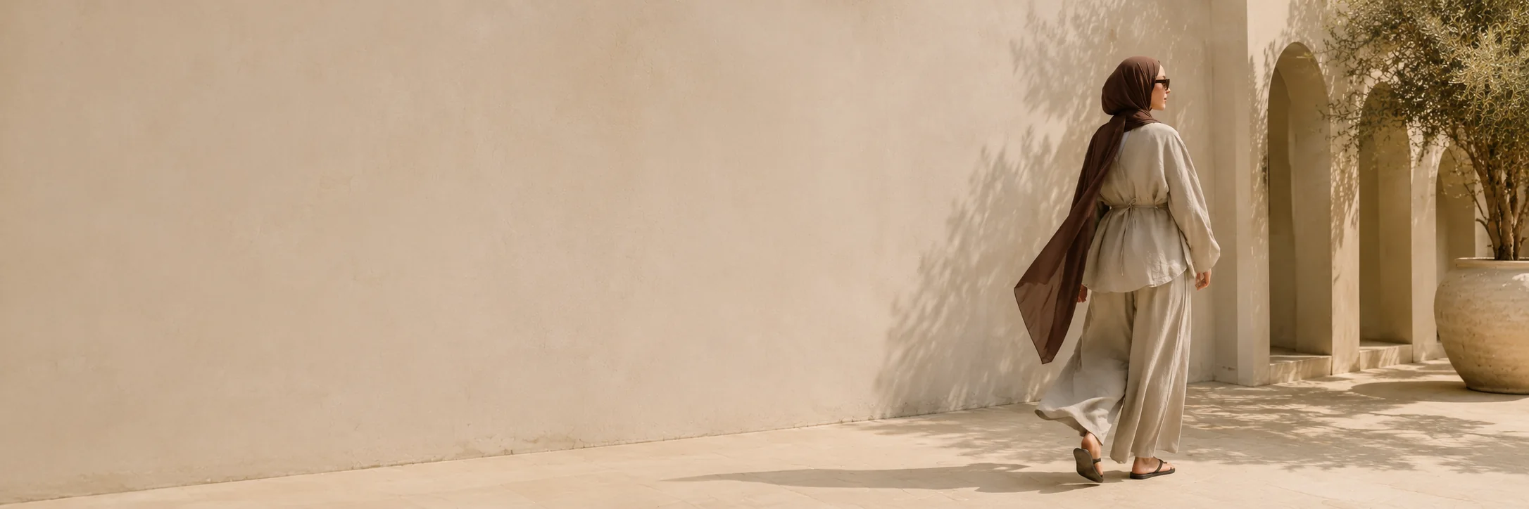 Woman wearing iStyle linen walking through a sunlit Mediterranean courtyard